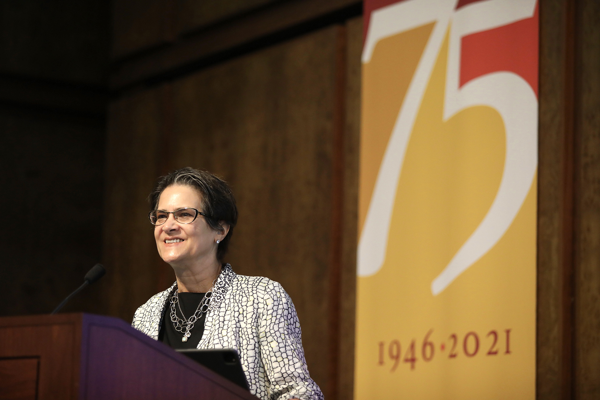 Martha S. Jones stands at the stage podium with the CMC 75th Anniversary banner behind her.