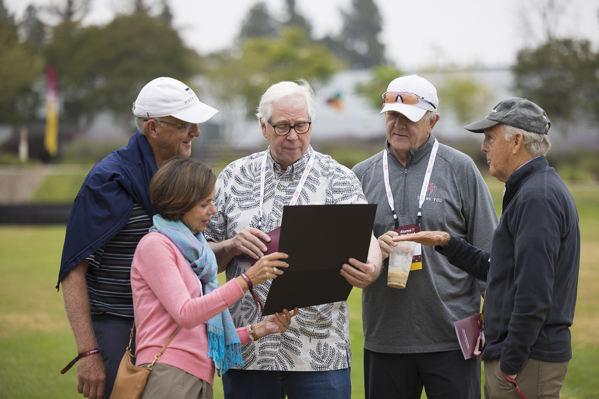 A group of alumni peer over to look at a certificate of recognition on Parents Field during 2022 Alumni Weekend 