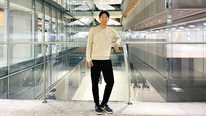 A student stands in front of a large open interior where several floors and escalators are visible