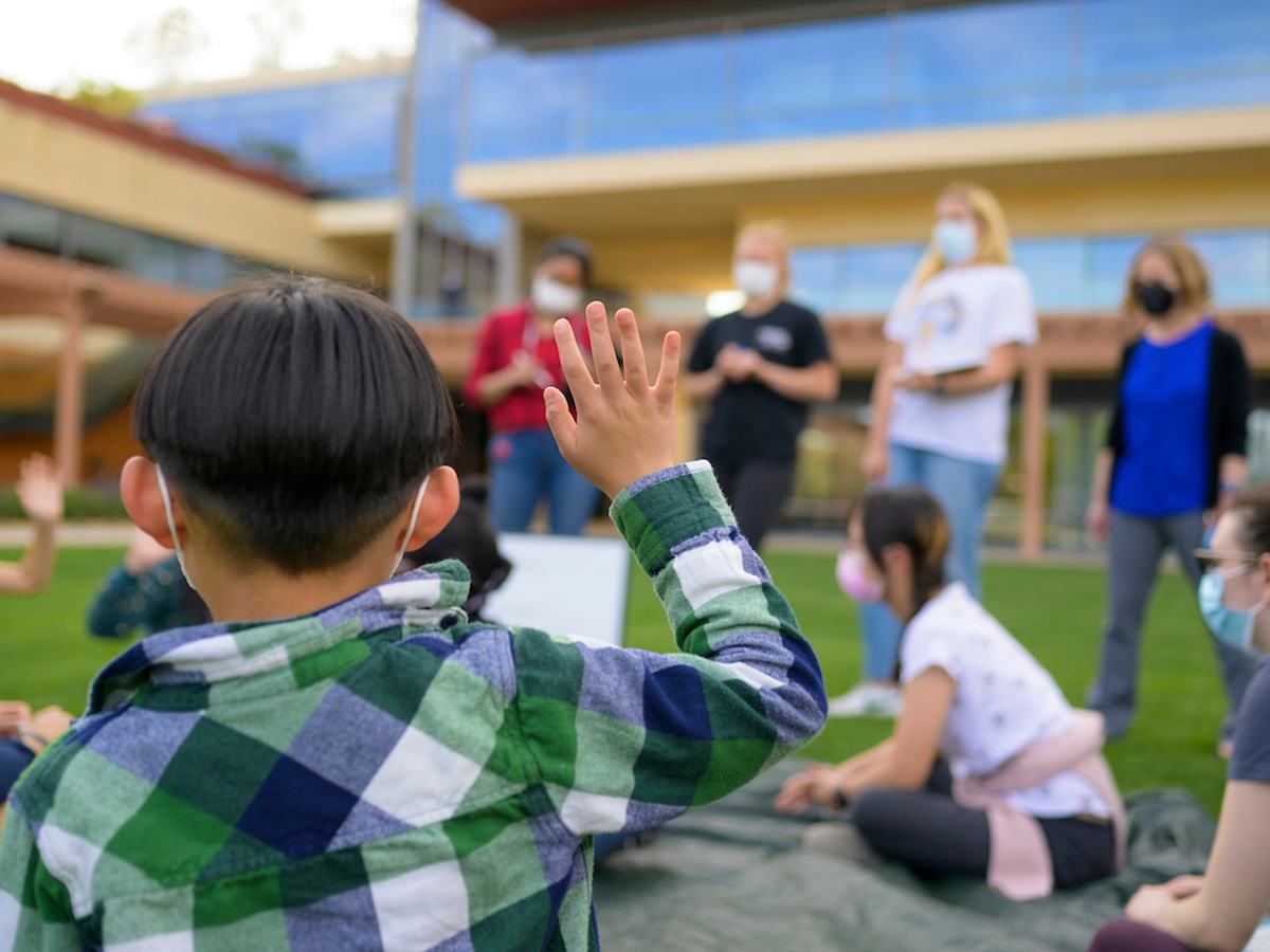A young child raising his hand in the foreground.