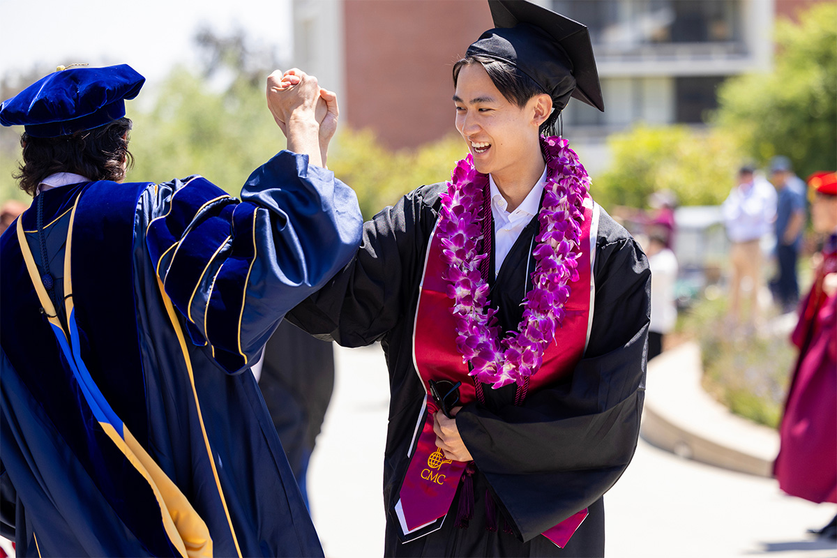 A male student high-fives a passing faculty member during Commencement.