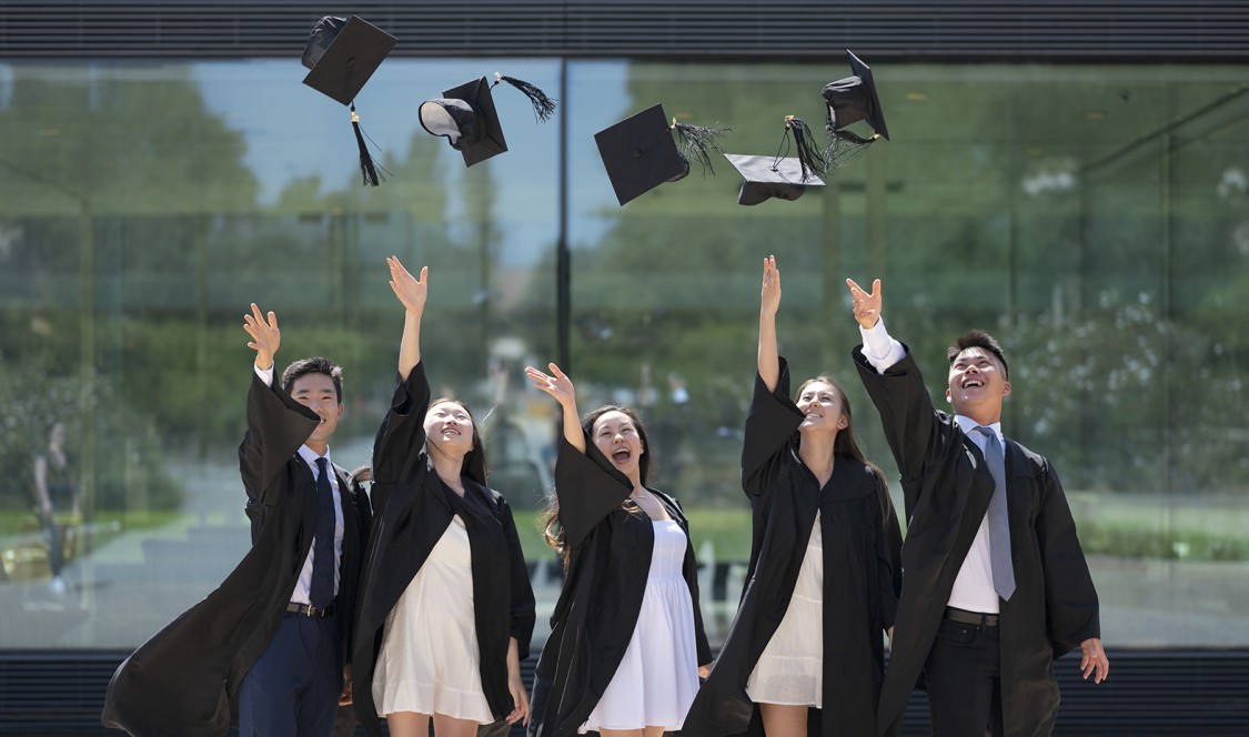 CMC graduates toss their mortar hats in front of the Kube for a photo opp in 2021.