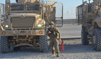 John posing in front of two military vehicles.