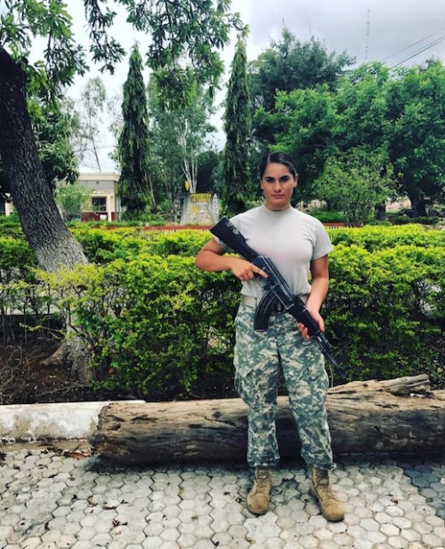 Hannah Alderete '20, dressed in military fatigues, holds a gun outdoors.