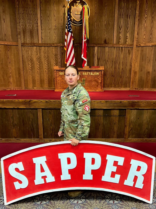 Lauren Jeans '24 holds a large "Sapper" sign in army fatigues.