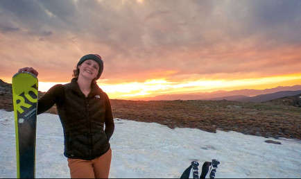 Robin Peterson '22 poses with her ski gear on a snowy mountain with the sunset behind her.