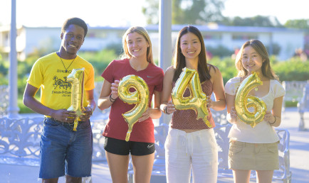 CMC students hold up gold mylar balloons reading "1946."