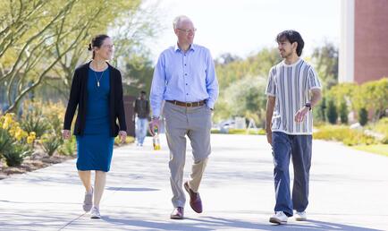 President Will Dudley and wife Dr. Carola Tanna walking with student on campus