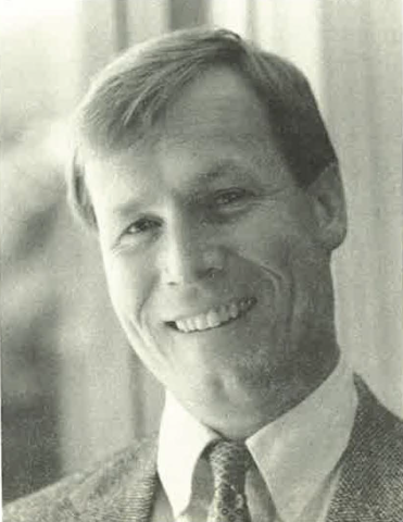 Black and white portrait of a young David Edwards smiling at the camera in suit jacket and tie.