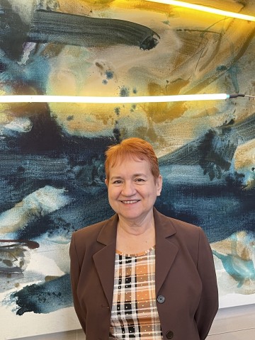 Portrait of Lydia Aguilar with her signature red hair, standing before the Mary Weatherford art inside Ath Eggert Dining Hall.